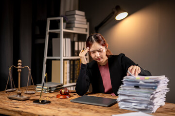 A woman is sitting at a desk with stacks of papers and a laptop