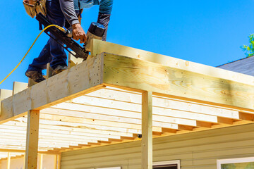 Worker installing beams with an air nail hammer nailing wooden planks