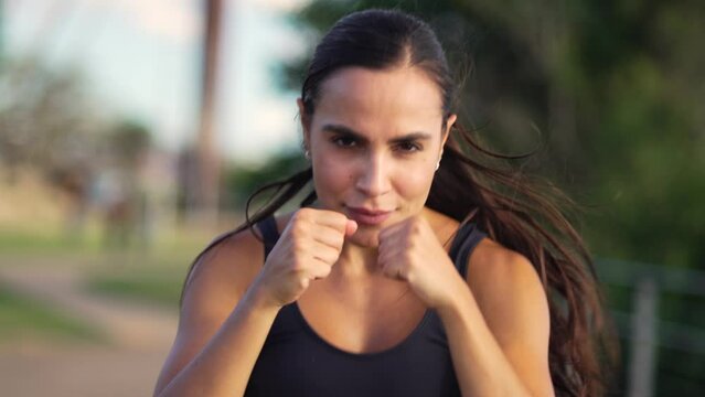 Determined female boxer practicing shadow boxing in front of the camera at an outdoor park. Intense gaze and precision punches from an athletic woman in a training session