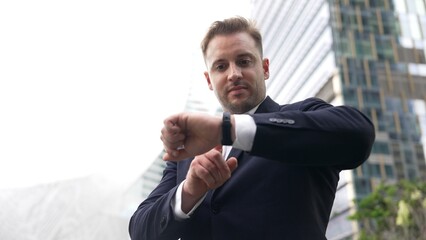 Low angle camera of businessman looking at watch to remind about time. Smart caucasian businessman...