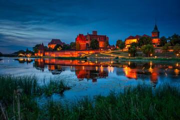 Obraz premium Castle of theTeutonic Order in Malbork by the Nogat river at dusk.
