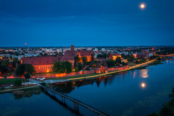Fototapeta premium Castle of theTeutonic Order in Malbork by the Nogat river at night with full moon.
