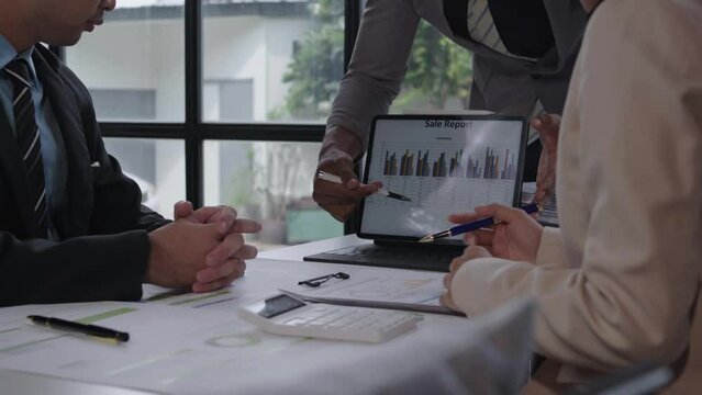 Colleagues analyzing sales data on a laptop screen, engaging in a business meeting, discussing strategies, and planning next steps in a modern office setting