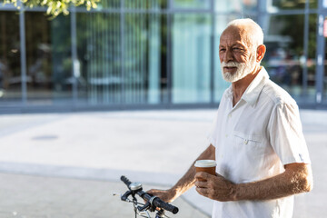 Casual handsome businessman going to work by bicycle. He is pushing bikeand drinking coffee to go.