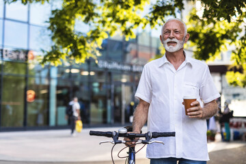 Casual handsome businessman going to work by bicycle. He is pushing bikeand drinking coffee to go.