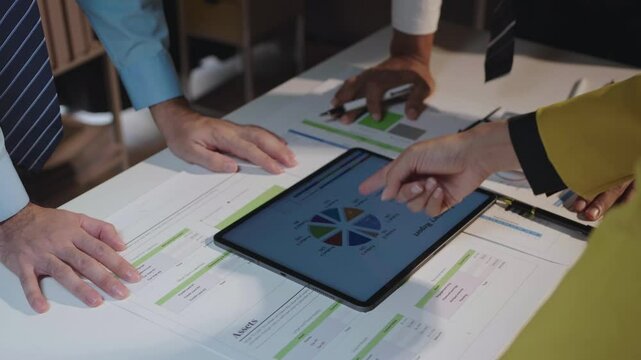 Business professionals collaborate around a tablet for data analysis, pointing at charts and discussing strategy in a conference room