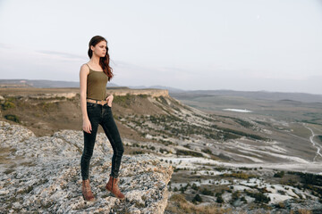 Woman in green top and jeans standing confidently on rock in serene valley landscape