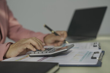 Happy young businesswoman in bright colored shirt uses computer and laptop in modern office Smiling manager while working on finance and marketing project Drink tea or coffee from a glass