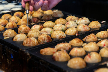 Cooking Takoyaki made of a wheat flour-based and cooked in a special molded in a shape of little round balls containing pieces of octopus. Famous street food in Japan.