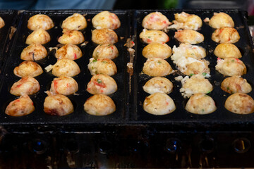 Cooking Takoyaki made of a wheat flour-based and cooked in a special molded in a shape of little round balls containing pieces of octopus. Famous street food in Japan.