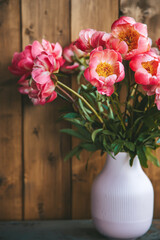 Gorgeous pink peonies in a pink ribbed vase with a wooden backdrop