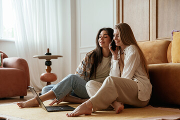 Eavesdrops on what saying on the phone. Two happy young female best friends are indoors