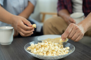 Selective focus, Hands of human picking up popcorn in plate on table during meeting with friends and enjoy eating together