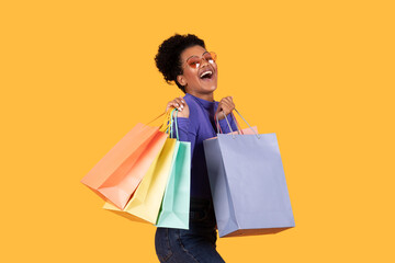 A woman with curly hair and heart-shaped sunglasses is smiling widely and holding several colorful...