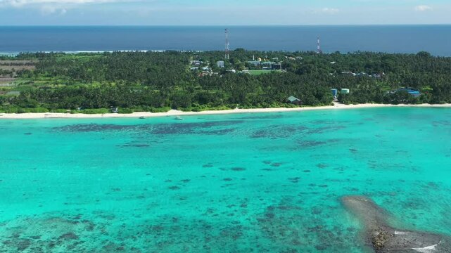 Aerial view of tranquil island life with lush greenery and coastal shoreline, Thoddoo Atoll, Maldives.