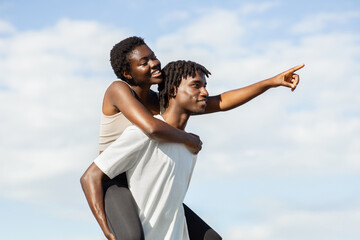 African American young couple is enjoying a sunny day together. The woman is riding piggyback on...