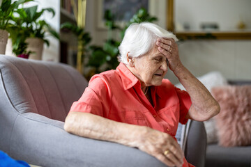 Elderly woman sitting in armchair suffering from headache 
