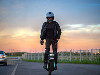 A man rides a monocycle against the background of a colorful summer sunset. He is equipped with a helmet, gloves and knee pads. Mobile urban transport © pavelkant