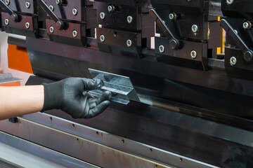 Close up the bending machine operator hold the sheet metal parts with rubber glove.