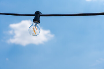 A light bulb against a clear blue sky with a white cloud. Concept of electricity saving idea.