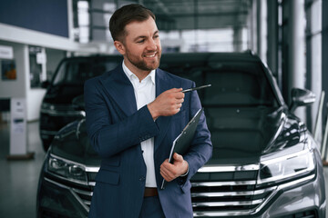 Cheerful salesman. Guy is in a car dealership