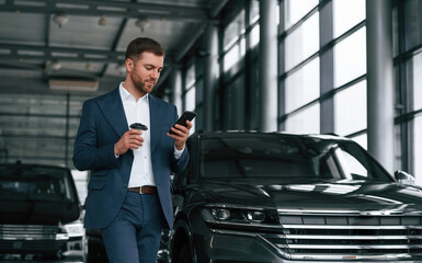 Break, with coffee and smartphone. A businessman is in a car dealership