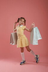 With shopping bags. Cute little girl is against pink background