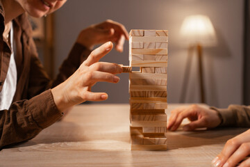 Friends playing wooden block game at home, close-up of hands stacking blocks