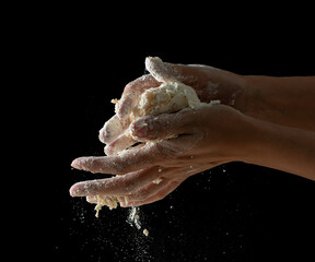 hands knead dough on a black background.