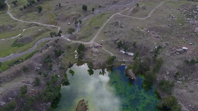 Aerial view of serene Naltar Valley with clear blue lake, lush greenery, and rocky terrain, Gilgit, Pakistan.
