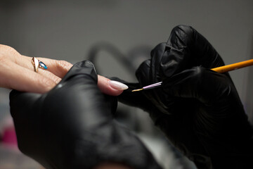  Close-up of a nail technician wearing black gloves, meticulously applying nail art with a fine...