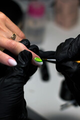 A professional manicurist in black gloves meticulously applies green nail art to a client's nails, emphasizing precision and creativity in a salon setting.