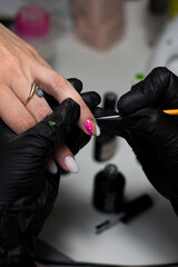 A professional manicurist in black gloves meticulously applying intricate nail art to a client’s nails, showcasing precision and creativity in a salon setting.