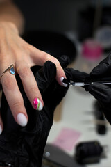  A professional manicurist in black gloves meticulously applies nail polish and designs to a client’s nails, showcasing precision and creativity in a salon setting.