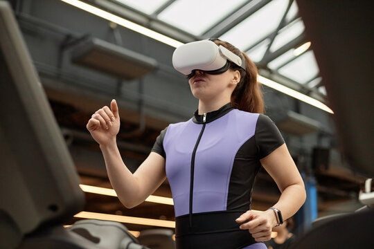 Waist up portrait of girl wearing VR headset running on treadmill in gym during immersive training session copy space