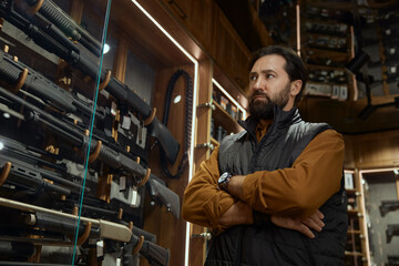 Adult pensive man choosing rifle gun looking at showcase in store