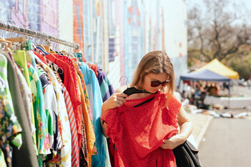 Portrait of a natural looking woman in 40s buying red dress on flea market. Garage sale, reuse the...