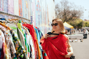 Portrait of a natural looking woman in 40s buying red dress on flea market. Garage sale, reuse the...