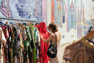 Portrait of a natural looking woman in 40s buying red dress on flea market. Garage sale, reuse the...