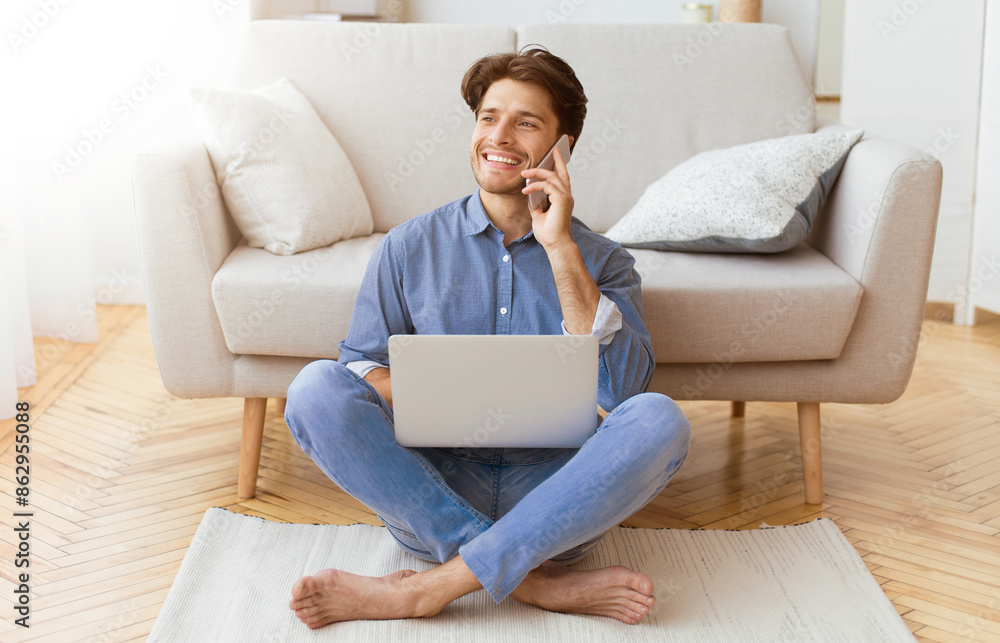 Poster a man sits on the floor in front of a couch, using a laptop and talking on his phone.