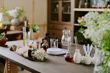 Medium close up of wooden table with glass flask full of essential oil and bouquet of white daisies