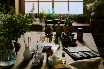Wooden table with small bottles of oils and vase with bouquet of greenery and black paper folder
