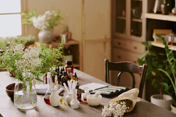 Perfumers wooden work desk with glass flasks with essence small brown glass bottles with essential oil and wildflowers