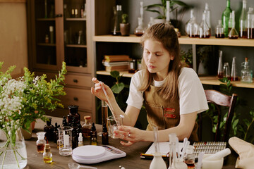 Female perfumer sitting at table and creating new scent while she mixing essential oils