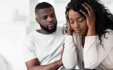 Obraz premium A man sits beside a woman who is upset and has her head in her hands. They are both indoors.