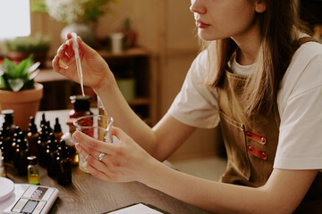 Medium close up of female perfumer adding new essential oil while she preparing new perfume for selling