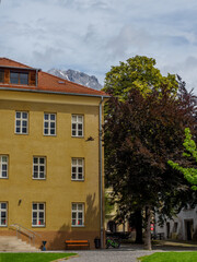 Naklejka premium Minimal photo of an old building and a tree in Tirol, Austria. Rocky mountain in the background. Photo taken from a park.