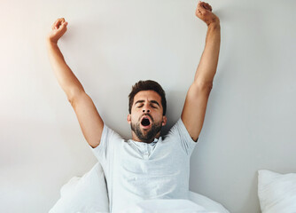 Wake up, yawn and tired man stretching in bed for burnout, fatigue or recovery at home on wall...
