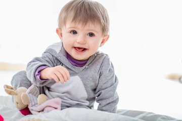 Adorable baby girl playing on bed with stuffed animal