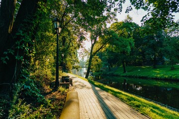 Scenic view of a park pathway alongside a tranquil river in Riga, Latvia